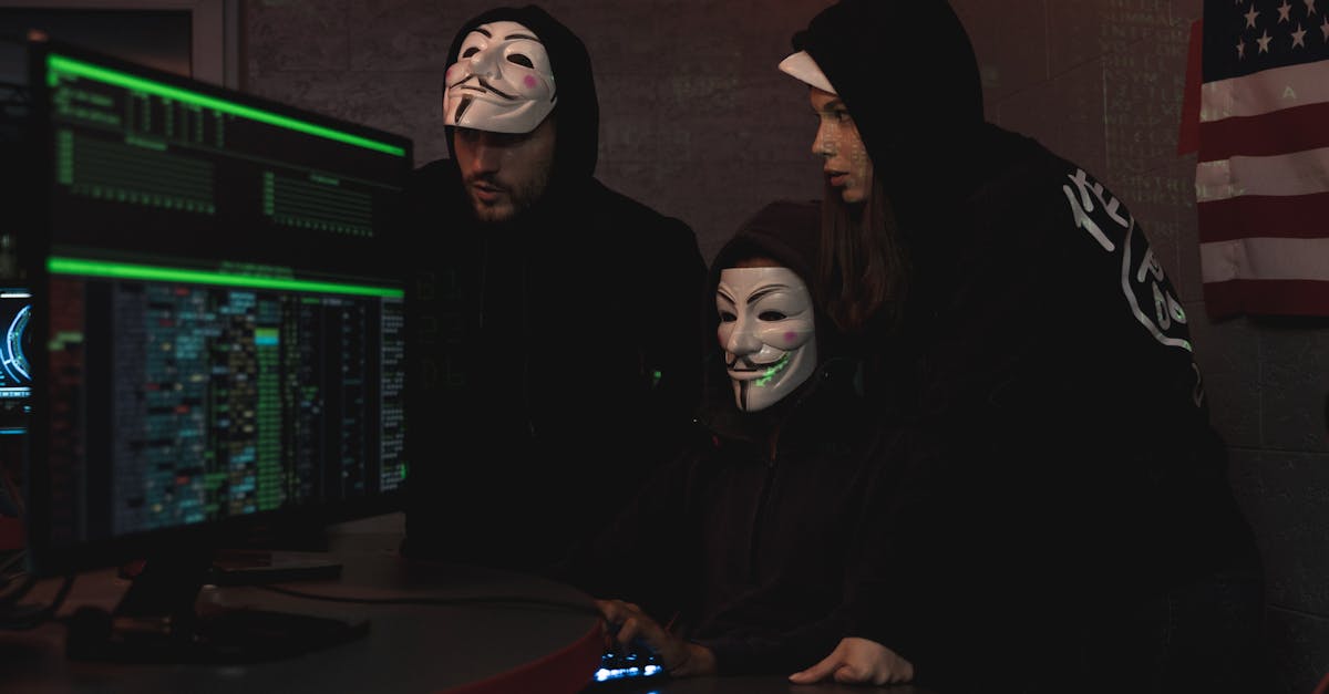 Masked hackers in hoodies working on a system in a dimly lit room, representing cyber security threats.