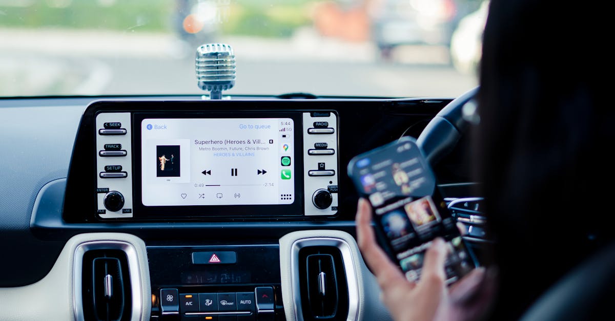 Car dashboard with a touchscreen display and person using a smartphone inside a vehicle.